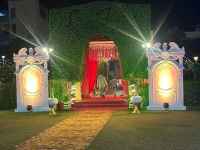 Green hedge arch entrance with white pillars and golden carpet path at Dharam Vatika, Sohna Gurgaon